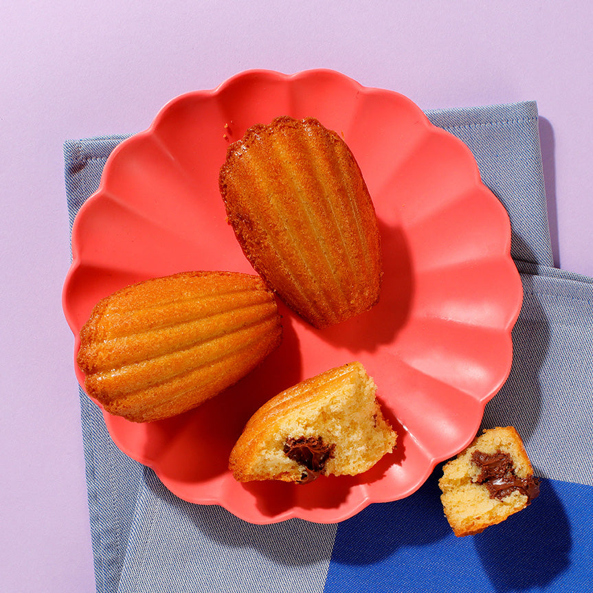 Three Choco-Hazelnute Madeleines on a plate viewed from above, one has been opened to show the filling inside