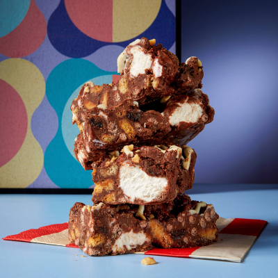 A stack of four Cake Club's Rocky Road slices on a red and white napkin sitting in front of a multi-patterned background.