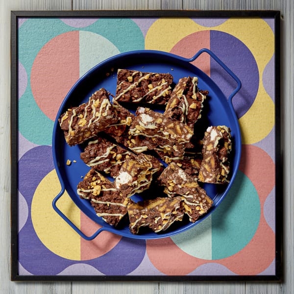 Overhead view of a tray of Cake Club's delicious Rocky Road on a round blue plate sitting on a multi-patterned background.