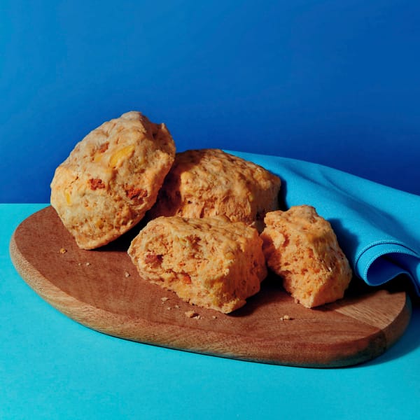 Three Vegan Cheeze and Facon Scones on a chopping board with a blue napkin on a contrasting blue background.
