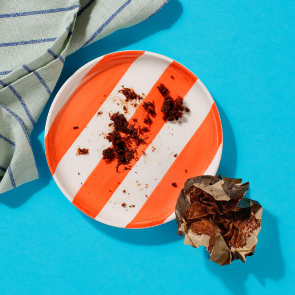 An empty plate except for a few crumbs and a wrapper from one of our Chocolate Muffins
