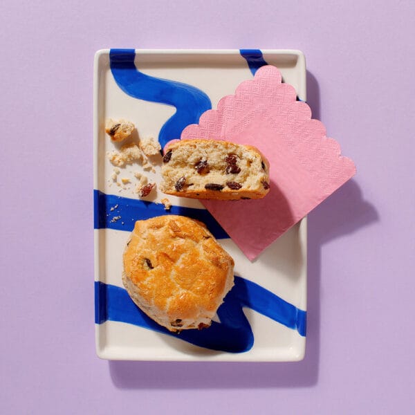 Close-up of The Big Sultana scone cut open on a patterned plate, showing soft crumb and juicy sultanas.