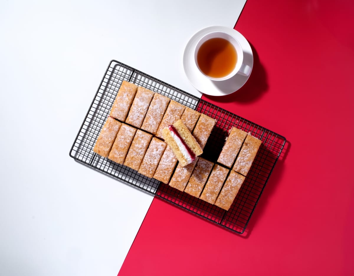 Overhead view of 18 slices of victoria sponge traycake on a red and white background.
