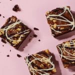 Square traybakes with crunchy tops and white drizzle on a pink background, illustrating the hybrid bakes and texture contrasts noted in cake trends for 2026.