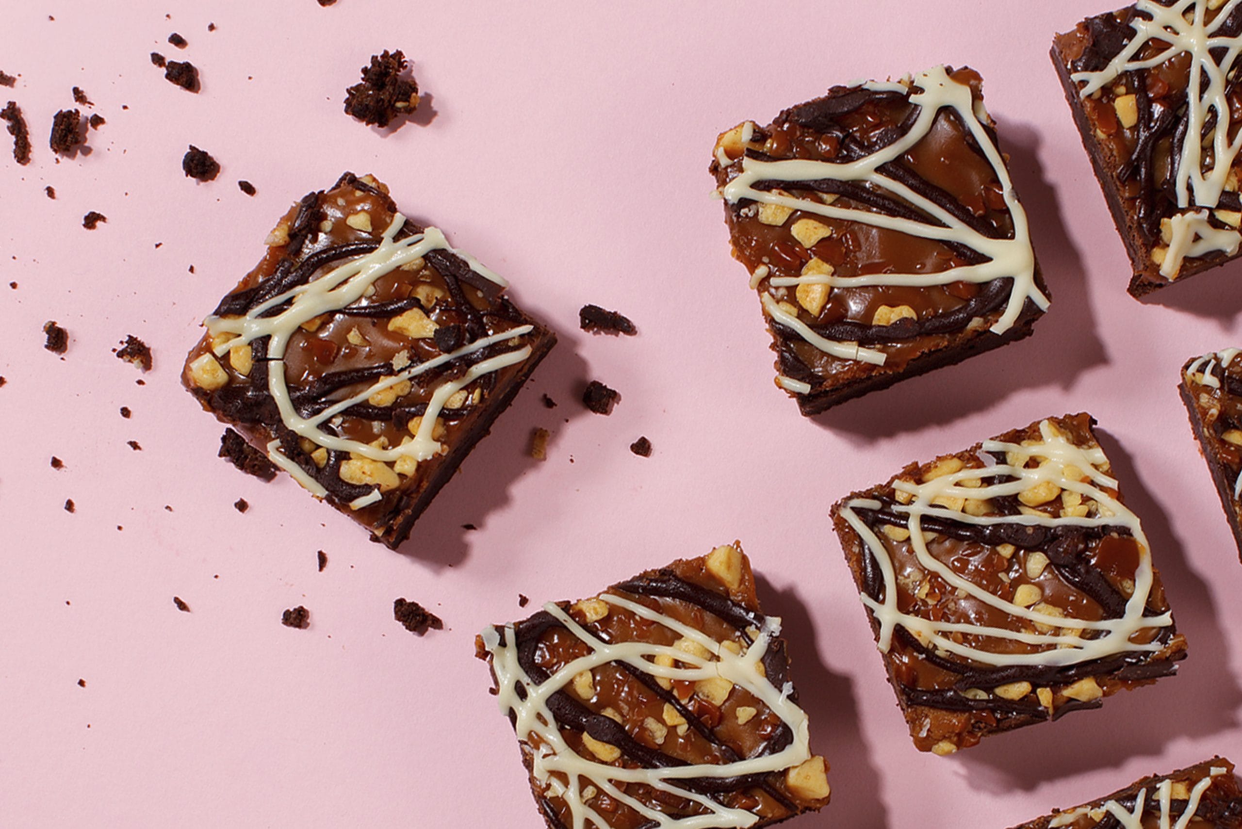 Square traybakes with crunchy tops and white drizzle on a pink background, illustrating the hybrid bakes and texture contrasts noted in cake trends for 2026.