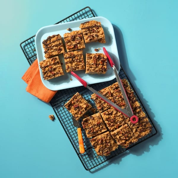 A whole tray of Maple and Pecan Flapjacks on a cooling rack and plate on a blue background.