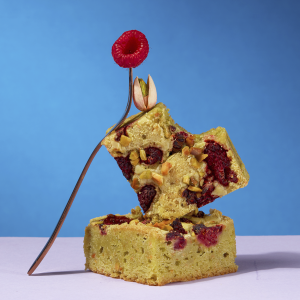 Pistachio and Raspberry Blondie square stacked with fresh raspberry garnish – golden, chewy blondie with pistachio crunch.