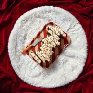 A decorated rum and raisin Christmas loaf cake on a red background, styled on a white faux fur mat.