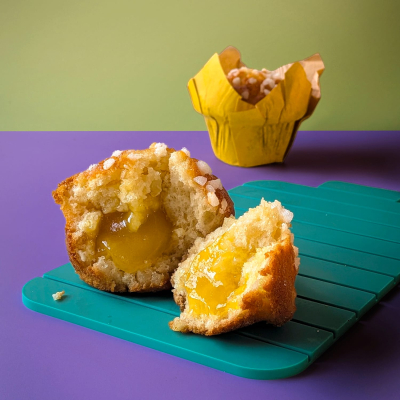 A Lemon and Apple Muffin broken in half on a green tray showing the delicious filling with another muffin in the background.