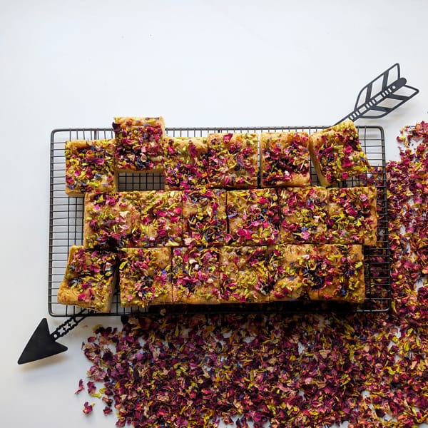 A full tray of Cake Club's Persian Love Cake on a cooling rack with a diagonal arrow and petals strewn across the background.