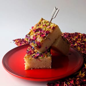 Angled view of a stack of three Persian Love Cakes on a red plate sitting on a bed of petals.