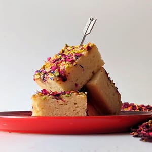 A side view of a stack of three Persian Love Cake on a red plate with a mini arrow embedded in the top.