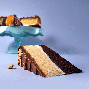 Side view of a slice of layered praline round cake with a blue cloche in the background on a purple surface