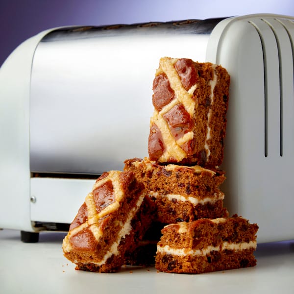 Four slices of Hot Cross Bun Traycake stacked on top of each other to the side of a white toaster.