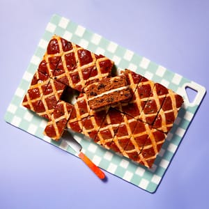 An overhead view of Cake Club's Hot Cross Bun Traycake on a checkered chopping board with a purple background.