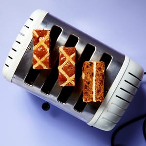 An overhead view of three slices of Hot Cross Bun Traycake on a white toaster with a purple background.
