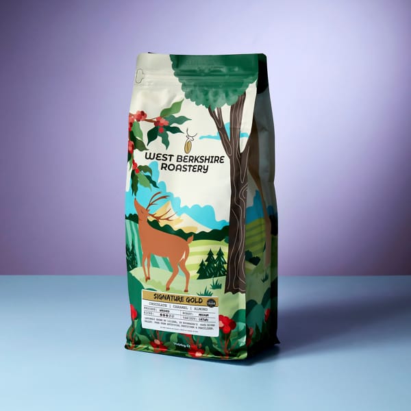 A 1kg bag of West Berkshire Roastery Signature Gold coffee beans on a light blue and purple contrasting background